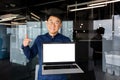 Portrait of smiling successful asian man inside office, man smiling and looking at camera standing holding laptop and Royalty Free Stock Photo
