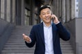 Portrait of a smiling and successful young Asian business man in a suit standing outside a building and talking on the Royalty Free Stock Photo