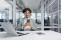 Portrait of a smiling and successful young businessman man in a suit sitting at a desk and using a mobile phone, looking Royalty Free Stock Photo