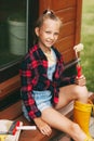 Portrait of a smiling teenage girl in denim overalls, plaid shirt, holding a roller in her hand. Close-up. Home improvement, DIY Royalty Free Stock Photo