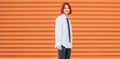 Portrait of smiling teenage girl with painted red dyed hair in white school shirt and necktie standing near orange wall background Royalty Free Stock Photo