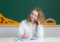 Portrait of smiling teenager girl over blackboard, friendly laughing. Cute college female student in hight school.