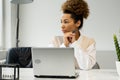 Portrait of a smiling, thoughtful woman sitting at an office desk with a laptop Royalty Free Stock Photo