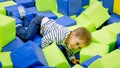 Portrait of smiling toddler boy crawling and having fun with soft cubes in amusement park