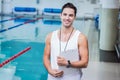 Male swim coach in tank top standing poolside holding clipboard wearing whistle near lane dividers Royalty Free Stock Photo