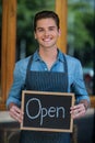 Portrait of smiling waiter showing chalkboard with open sign