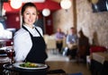 Portrait of smiling waitress with serving tray meeting restaurant guests