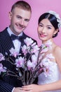 Portrait of smiling wedding couple holding artificial flowers against pink background Royalty Free Stock Photo