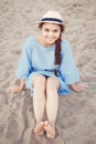 Portrait of smiling white Caucasian brunette woman with tanned skin in blue dress and straw hat sitting on sand beach shore Royalty Free Stock Photo