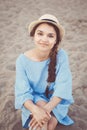 Portrait of smiling white Caucasian brunette woman with tanned skin in blue dress and straw hat sitting on sand beach shore Royalty Free Stock Photo