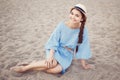 Portrait of smiling white Caucasian brunette woman with tanned skin in blue dress and straw hat sitting on sand beach shore Royalty Free Stock Photo