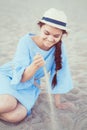 Portrait of smiling white Caucasian brunette woman with tanned skin in blue dress and straw hat sitting on sand beach Royalty Free Stock Photo