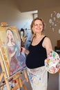 Portrait of smiling white Caucasian young pregnant woman drawing painting standing at easel in home studio, art