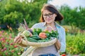 Portrait of smiling woman with basket of different fresh vegetables and herbs