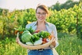 Portrait of smiling woman with basket of different fresh vegetables and herbs