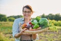 Portrait of smiling woman with basket of different fresh vegetables and herbs