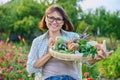 Portrait of smiling woman with basket of different fresh vegetables and herbs