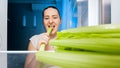 Portrait of smiling young woman biting piece of celery at night