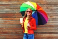 Portrait smiling woman with coffee cup and colorful umbrella in autumn day over wooden background wearing red leather jacket Royalty Free Stock Photo