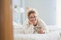 Portrait of smiling woman in eyeglasses and curly hair lying on comfortable bed with coffee cup at home. Happy woman having Royalty Free Stock Photo