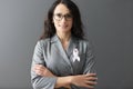 Portrait of smiling woman in gray suit on her chest with pink ribbon symbol of fight against breast cancer