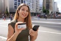 Portrait of smiling woman holding a smartphone and showing a credit card looking at camera on Paulista Avenue financial center of Royalty Free Stock Photo