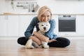 Woman hugging little dog while posing on floor in kitchen Royalty Free Stock Photo