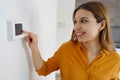 Portrait of smiling woman lowers the temperature on digital thermostat at home. Energy saving, efficient and smart technology Royalty Free Stock Photo