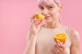 Portrait of smiling woman with pink hair holding half of ripe orange and smelling fresh lemon, posing isolated over pink Royalty Free Stock Photo