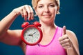 A portrait of smiling woman in sportswear holding alarm clock. People, fitness and healthcare concept Royalty Free Stock Photo