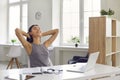 Portrait of a smiling woman sitting in the office in front of a laptop and stretching after work. Royalty Free Stock Photo