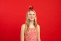 Portrait of smiling wonderful teenage girl with fair hair holding balancing big red apple on head on red background. Royalty Free Stock Photo