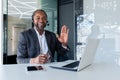 Portrait of a smiling young African American man in a suit sitting at a desk in a headset and in front of a laptop Royalty Free Stock Photo