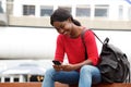 Smiling young african american woman sitting outside in the city with bag and cellphone Royalty Free Stock Photo