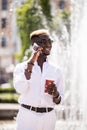 Portrait of smiling young afro american man talking on mobile phone and drinking phone while standing near the fountain in the cit Royalty Free Stock Photo