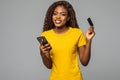 Portrait of a smiling young afro american woman holding mobile phone and showing credit cards over white background Royalty Free Stock Photo