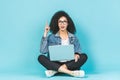 Portrait of smiling young afro american woman using laptop while sitting on a floor with legs crossed isolated over blue Royalty Free Stock Photo