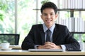 Portrait of smiling young Asian businessman sitting at office working desk, his hands are on laptop computer Royalty Free Stock Photo