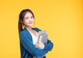 Portrait of smiling young Asian girl college student with laptop and book isolated over yellow background Royalty Free Stock Photo