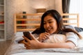 Portrait of smiling young Asian girl lying down on bed while making a video call in bedroom at home. Video conferencing Royalty Free Stock Photo