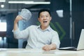 Portrait of a smiling young Asian man businessman sitting in the office in front of the camera and showing a fan of cash Royalty Free Stock Photo