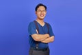 Portrait of smiling young Asian man crossing his arms and wearing glasses on purple background Royalty Free Stock Photo