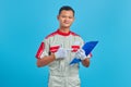 Portrait of smiling young Asian mechanic pointing at clipboard with finger over blue background