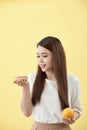 Portrait of a smiling young asian woman choosing between donut and orange isolated over yellow background Royalty Free Stock Photo