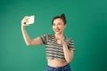 Portrait of smiling young Asian woman holding smartphone in hand shooting selfie over green background