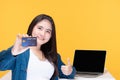 Portrait of smiling young beautiful woman holding a credit card in front of the laptop blank screen on yellow background. Shopping Royalty Free Stock Photo