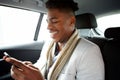 Smiling young black man looking at cellphone while in backseat of car Royalty Free Stock Photo