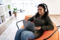 Smiling black woman in headset using laptop at home