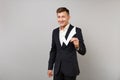 Portrait of smiling young business man in classic black suit, white shirt holding check mark isolated on grey wall Royalty Free Stock Photo