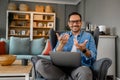 Portrait of smiling young businessman gesturing while sitting with laptop on armchair at home office Royalty Free Stock Photo